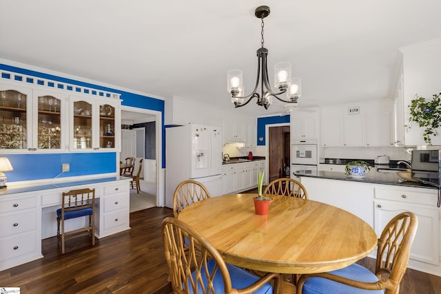 dining room featuring dark wood-type flooring, built in study area, ornamental molding, and a notable chandelier