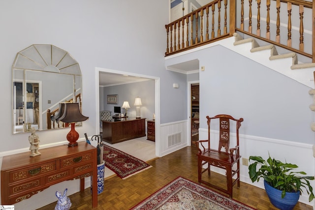 entryway featuring a wainscoted wall, visible vents, a towering ceiling, ornamental molding, and stairs