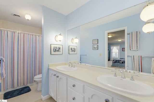 ensuite bathroom featuring toilet, double vanity, visible vents, and a sink