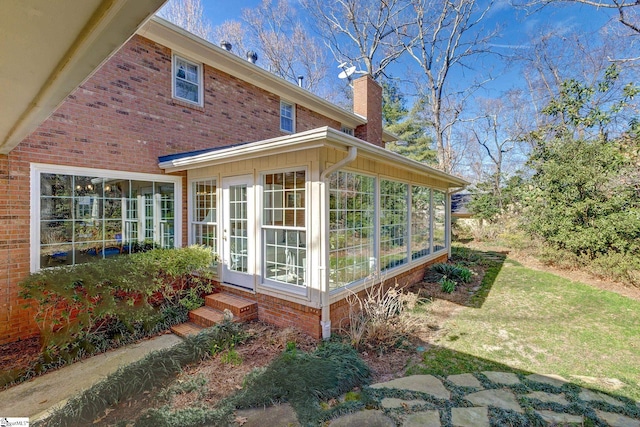 view of home's exterior featuring a sunroom, brick siding, and a chimney