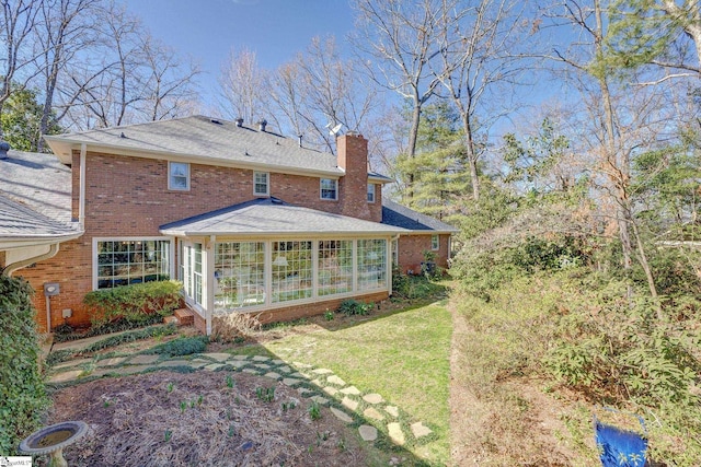 rear view of property with a yard, a sunroom, a chimney, and brick siding