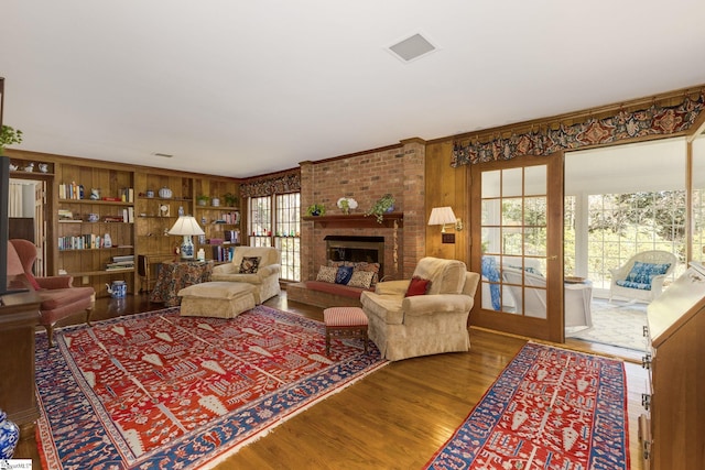 living room with visible vents, wood finished floors, wood walls, a brick fireplace, and built in shelves