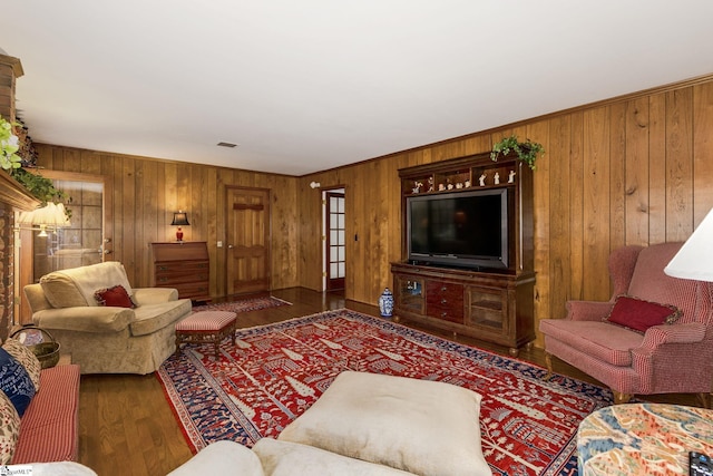 living room with crown molding, wooden walls, visible vents, and wood finished floors