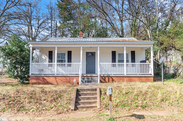 view of front of house featuring covered porch, metal roof, and a chimney