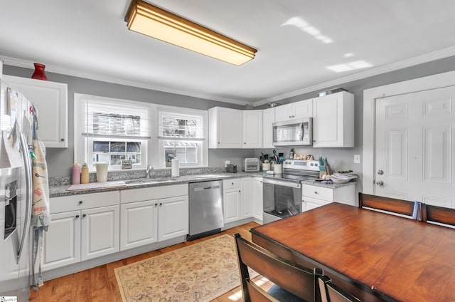 kitchen with stainless steel appliances, crown molding, a sink, and light wood finished floors