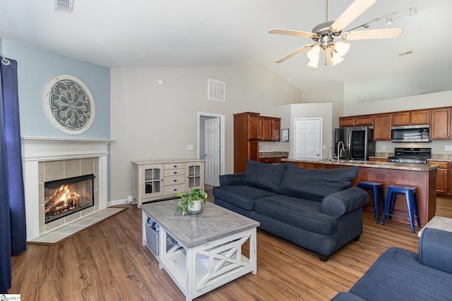 living area featuring visible vents, a fireplace, light wood-style flooring, and ceiling fan