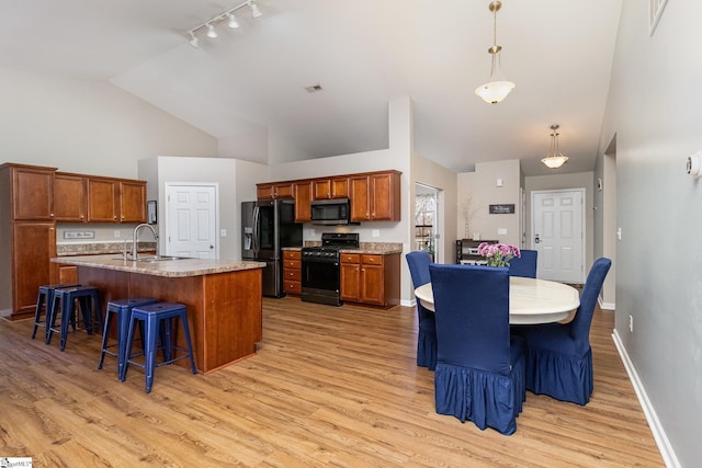 kitchen featuring brown cabinets, light wood-type flooring, black appliances, a kitchen bar, and a sink