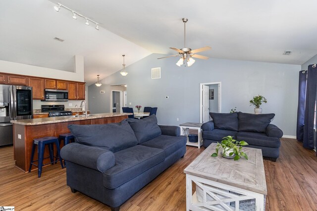 living area featuring light wood-style flooring, visible vents, vaulted ceiling, and a ceiling fan