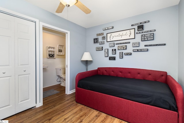 bedroom featuring connected bathroom, a ceiling fan, wainscoting, wood finished floors, and a closet