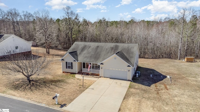 view of front of property featuring a shingled roof, covered porch, concrete driveway, a garage, and a forest view