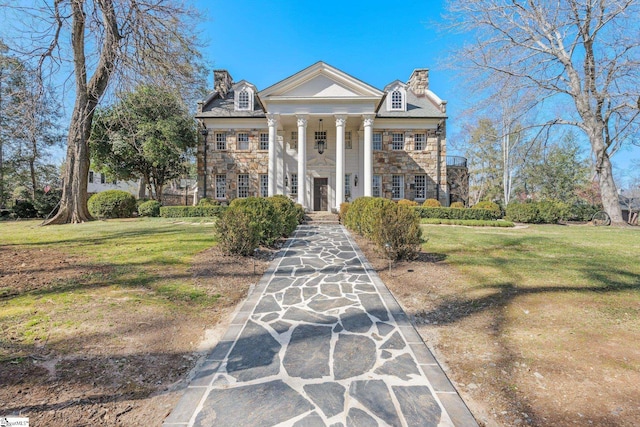 neoclassical / greek revival house with stone siding, a chimney, and a front lawn