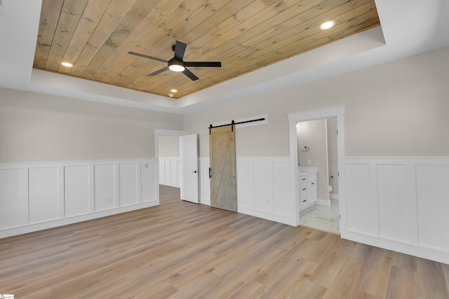 unfurnished bedroom featuring a raised ceiling, light wood-style flooring, a barn door, wood ceiling, and connected bathroom