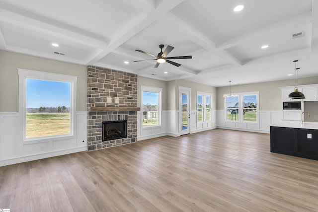 unfurnished living room featuring light wood-style floors, beam ceiling, visible vents, and a stone fireplace