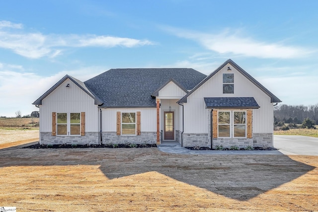 modern farmhouse with a shingled roof, stone siding, and board and batten siding