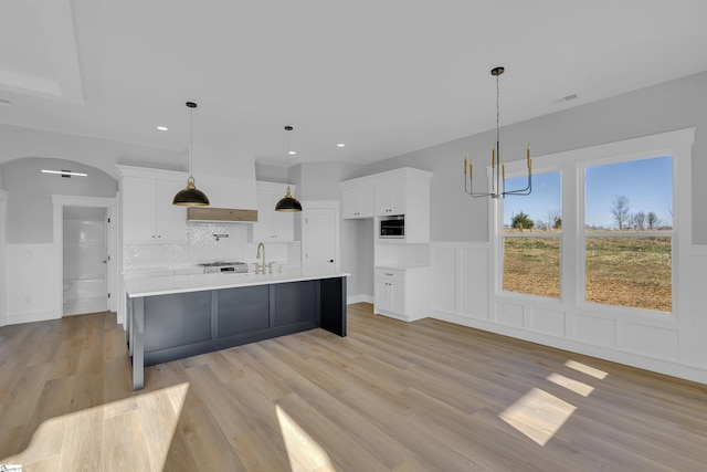 kitchen featuring arched walkways, light countertops, light wood-style flooring, and white cabinetry