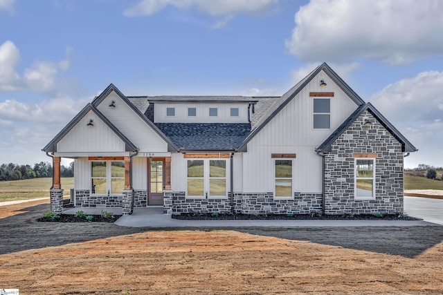 rear view of property with covered porch, stone siding, roof with shingles, and board and batten siding