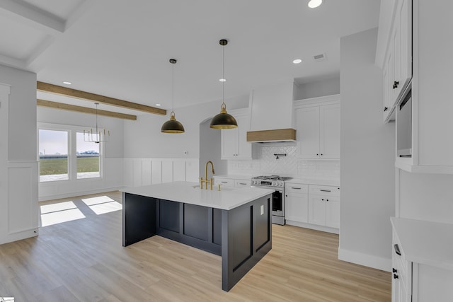 kitchen with stainless steel gas stove, wainscoting, beamed ceiling, light countertops, and premium range hood