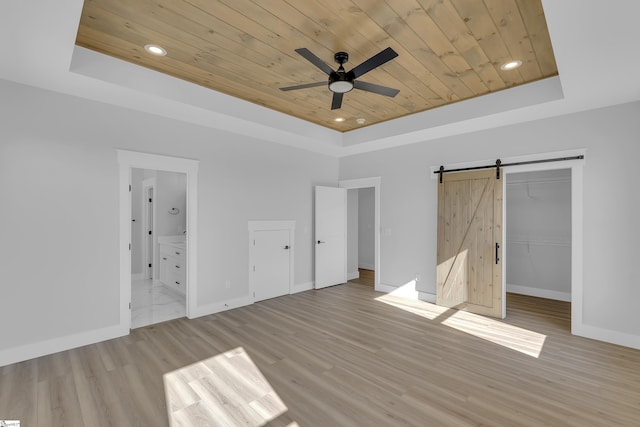 unfurnished bedroom featuring wooden ceiling, a barn door, baseboards, and a raised ceiling