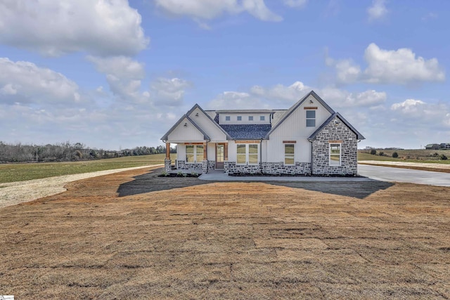 view of front of property featuring a front yard, stone siding, and covered porch