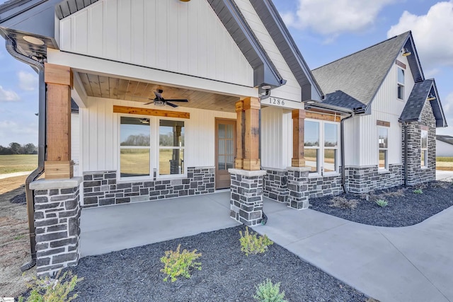 doorway to property featuring stone siding, ceiling fan, and roof with shingles