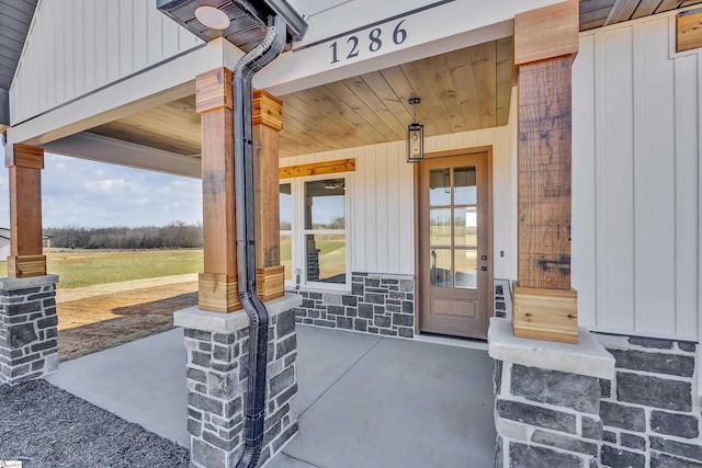 doorway to property featuring covered porch, stone siding, and board and batten siding