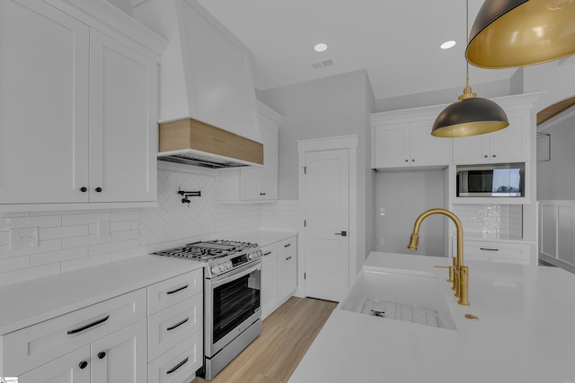 kitchen featuring stainless steel gas range oven, white cabinets, light countertops, premium range hood, and a sink