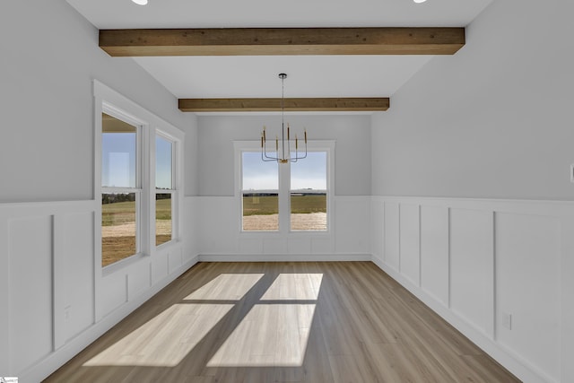 unfurnished dining area with a wainscoted wall, beamed ceiling, wood finished floors, and an inviting chandelier