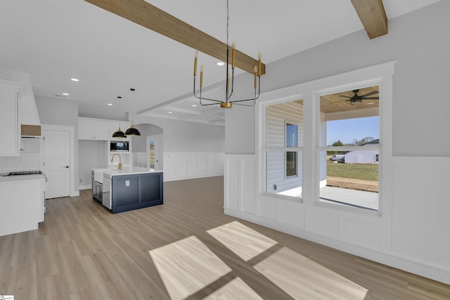 kitchen featuring arched walkways, light countertops, open floor plan, white cabinets, and beamed ceiling