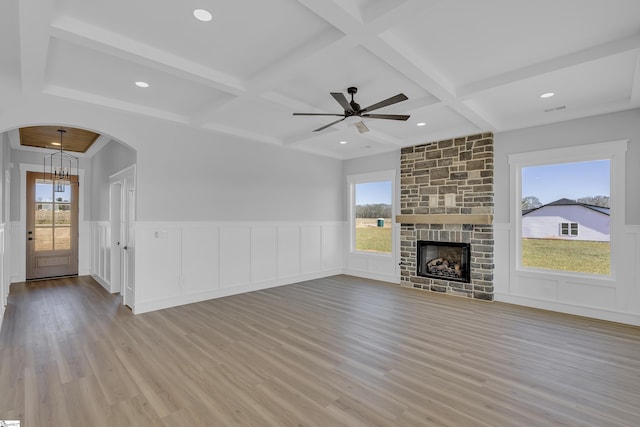 unfurnished living room featuring a fireplace, arched walkways, coffered ceiling, and a wealth of natural light