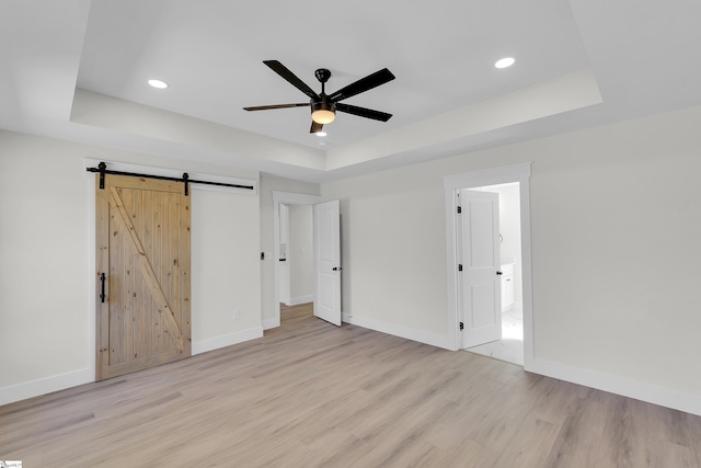 unfurnished bedroom featuring a tray ceiling, a barn door, and light wood-style floors