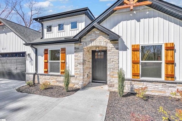 doorway to property with a garage, stone siding, a shingled roof, and board and batten siding