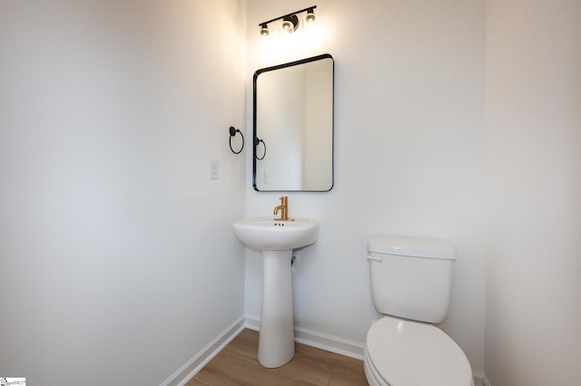 half bath featuring baseboards, toilet, and wood finished floors