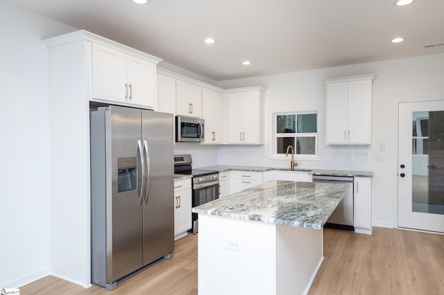 kitchen featuring stainless steel appliances, tasteful backsplash, light wood-style floors, a sink, and a kitchen island