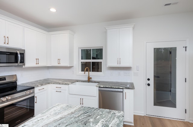 kitchen with light stone counters, a sink, visible vents, white cabinets, and appliances with stainless steel finishes