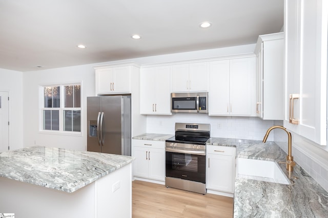 kitchen with light stone counters, light wood-style flooring, a sink, white cabinets, and appliances with stainless steel finishes