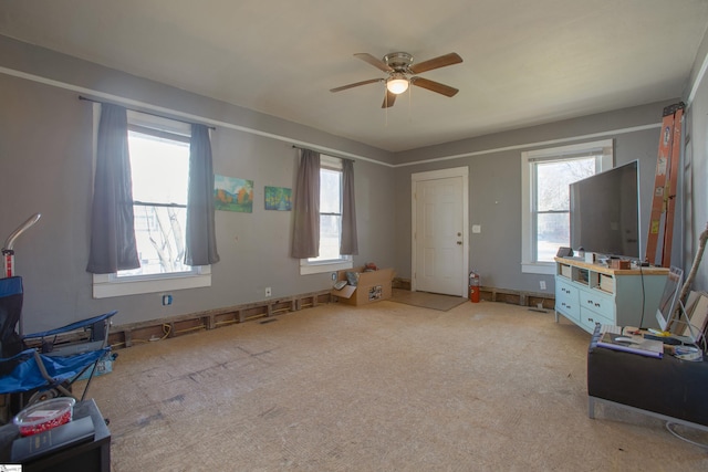 living area with a ceiling fan, light colored carpet, and a healthy amount of sunlight