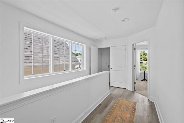 hall with wood finished floors, an upstairs landing, and baseboards