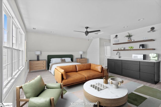 bedroom featuring light wood finished floors, ceiling fan, vaulted ceiling, and a sink