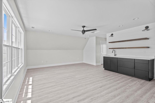 interior space featuring a sink, a ceiling fan, baseboards, vaulted ceiling, and light wood-type flooring