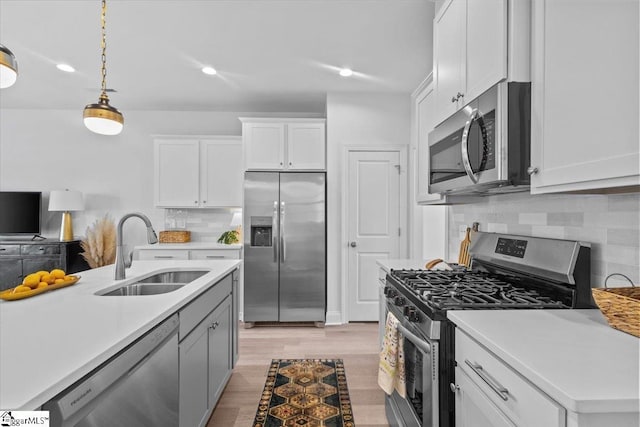 kitchen featuring light countertops, hanging light fixtures, appliances with stainless steel finishes, white cabinets, and a sink