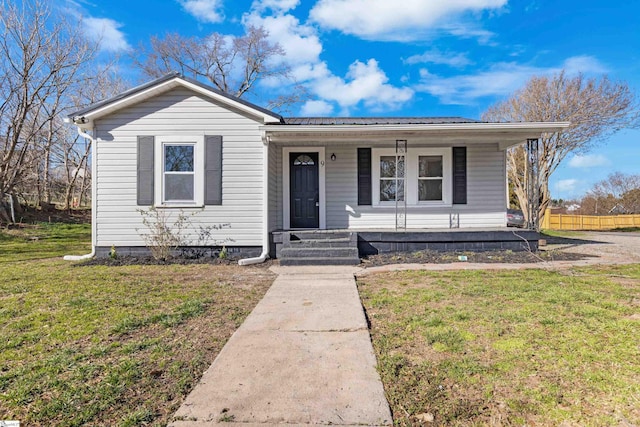 bungalow-style home featuring metal roof, a porch, fence, and a front lawn