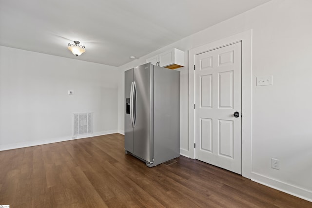 kitchen featuring dark wood-type flooring, stainless steel fridge, visible vents, and white cabinets