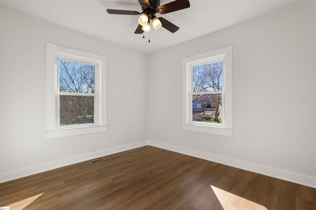 spare room with dark wood-type flooring, visible vents, ceiling fan, and baseboards