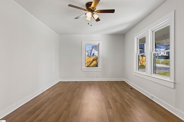 spare room featuring baseboards, dark wood-style flooring, and a wealth of natural light