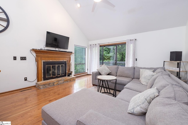 living area featuring visible vents, a stone fireplace, wood finished floors, high vaulted ceiling, and baseboards