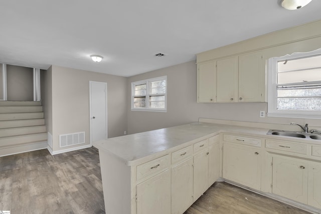 kitchen with light countertops, visible vents, light wood-style floors, a sink, and a peninsula