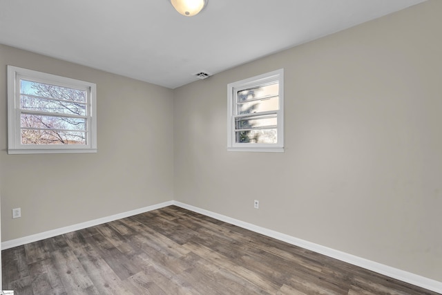 empty room with dark wood-type flooring, visible vents, and baseboards