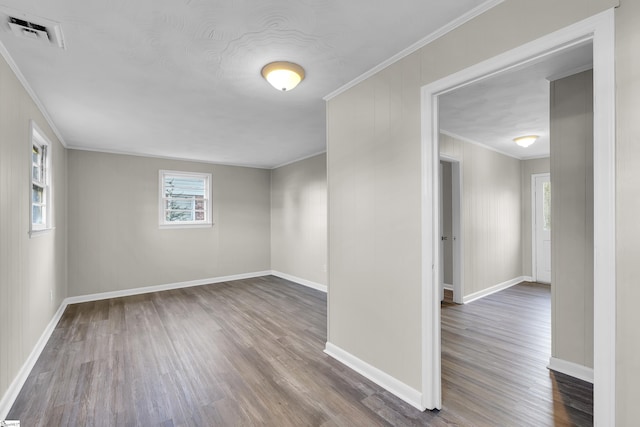 empty room with baseboards, wood finished floors, visible vents, and crown molding