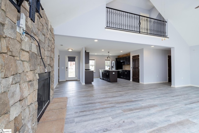 unfurnished living room featuring a towering ceiling, light wood finished floors, baseboards, and a stone fireplace