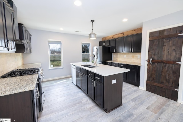 kitchen with a center island with sink, light countertops, appliances with stainless steel finishes, light wood-style floors, and a sink